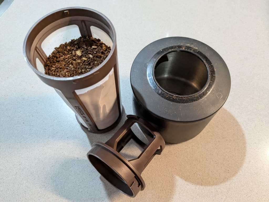filter holding ground coffee and an empty black metal cup