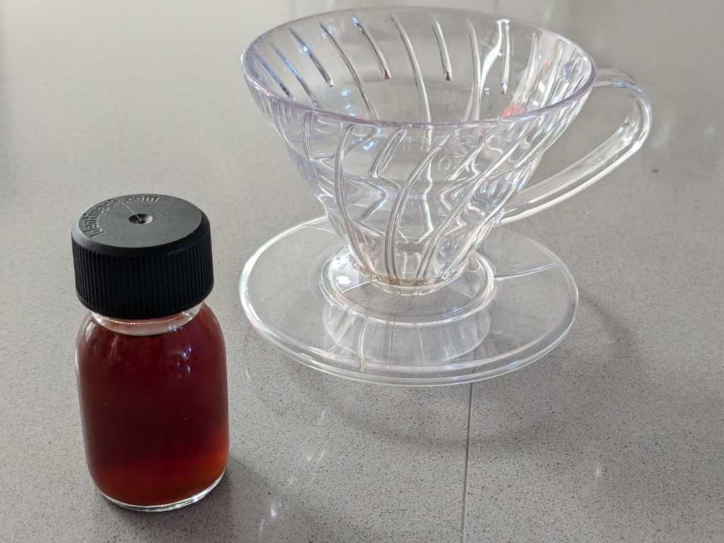 glass sample bottle with a dose of cold brew coffee shown against a size 1 hario v60 filter holder